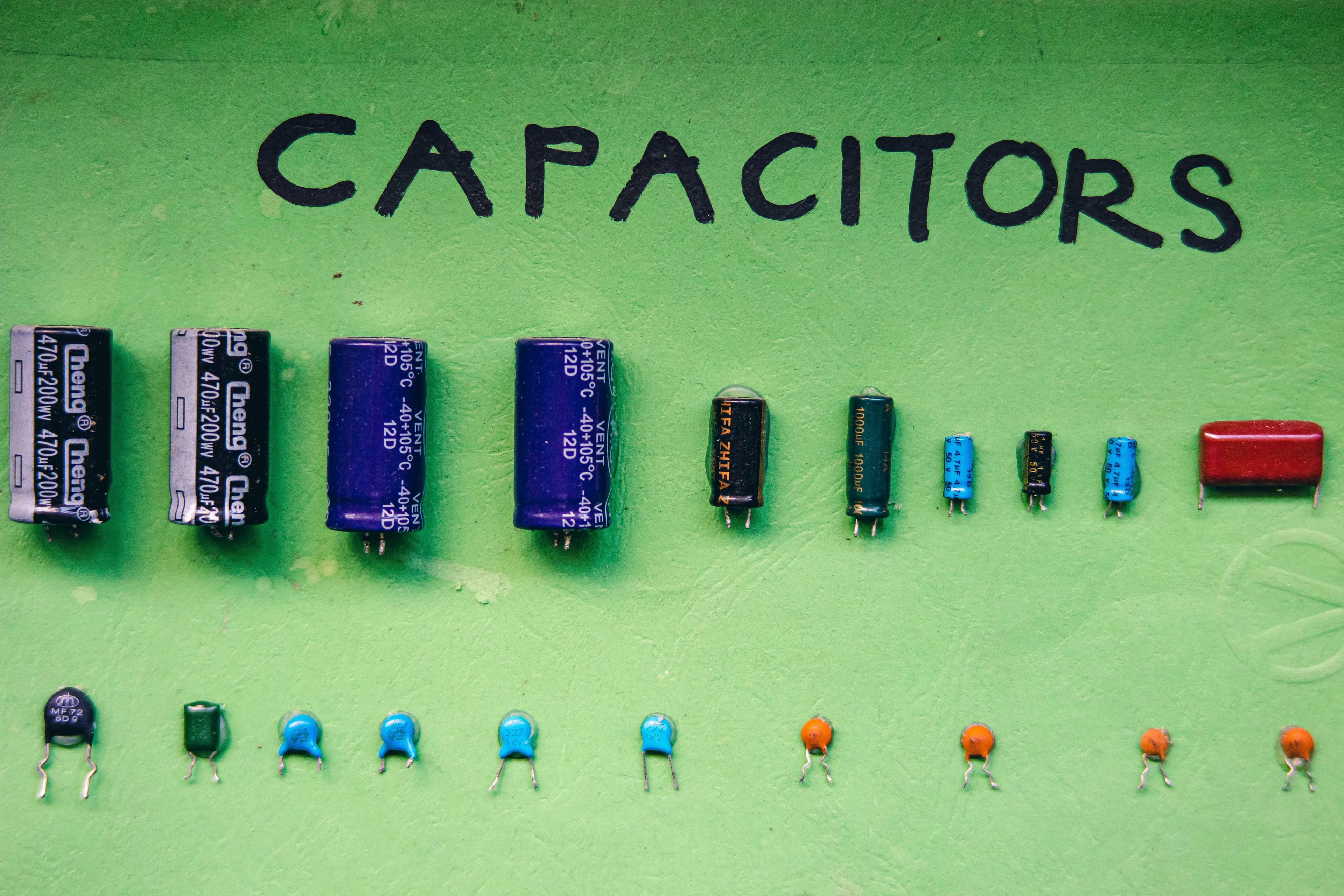 Top view layout of various capacitors for storing electrical energy of different sizes and capacities arranged on green background with inscription