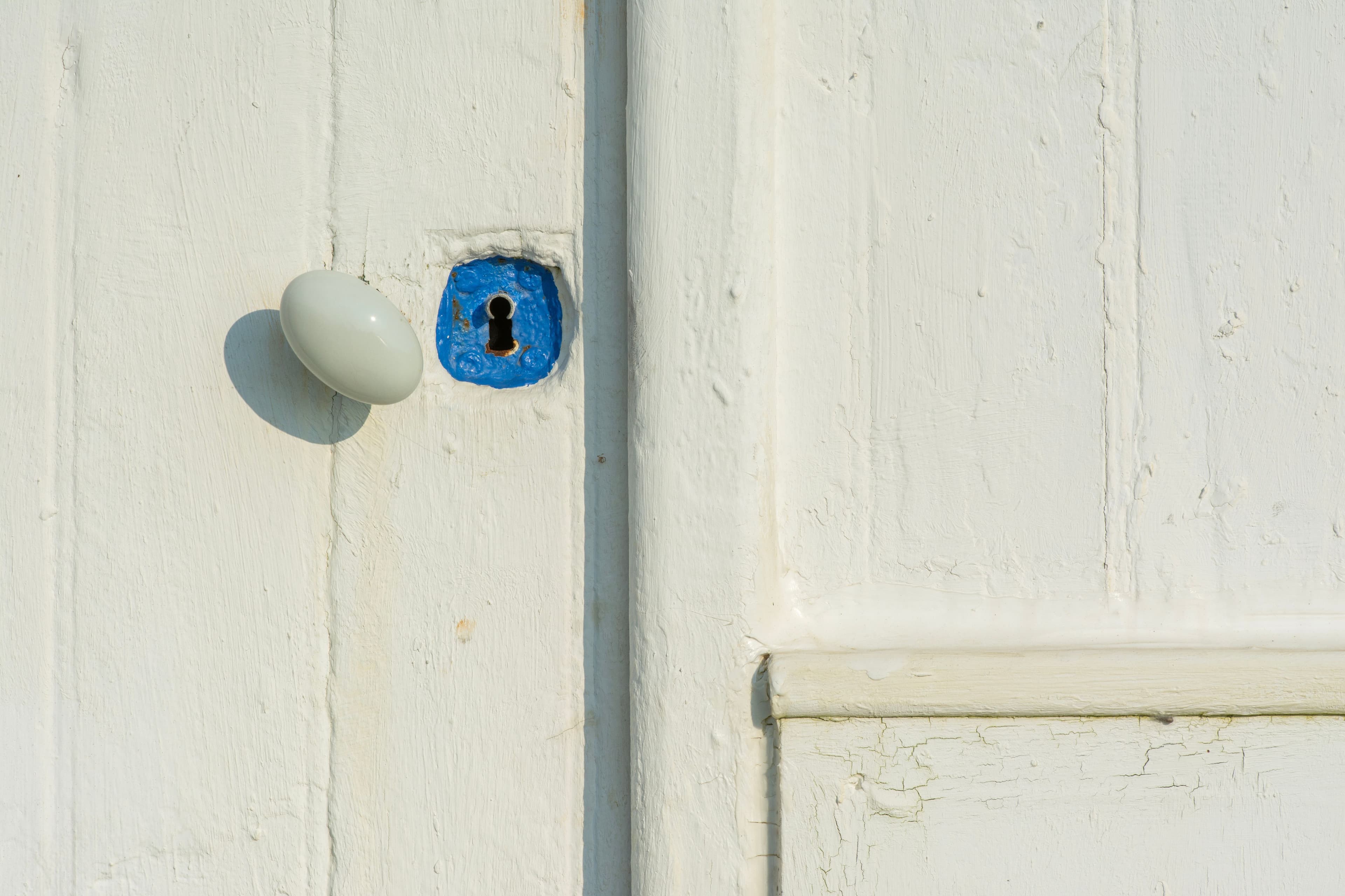 Close-up of an old rustic white door with a blue keyhole and charming patina.