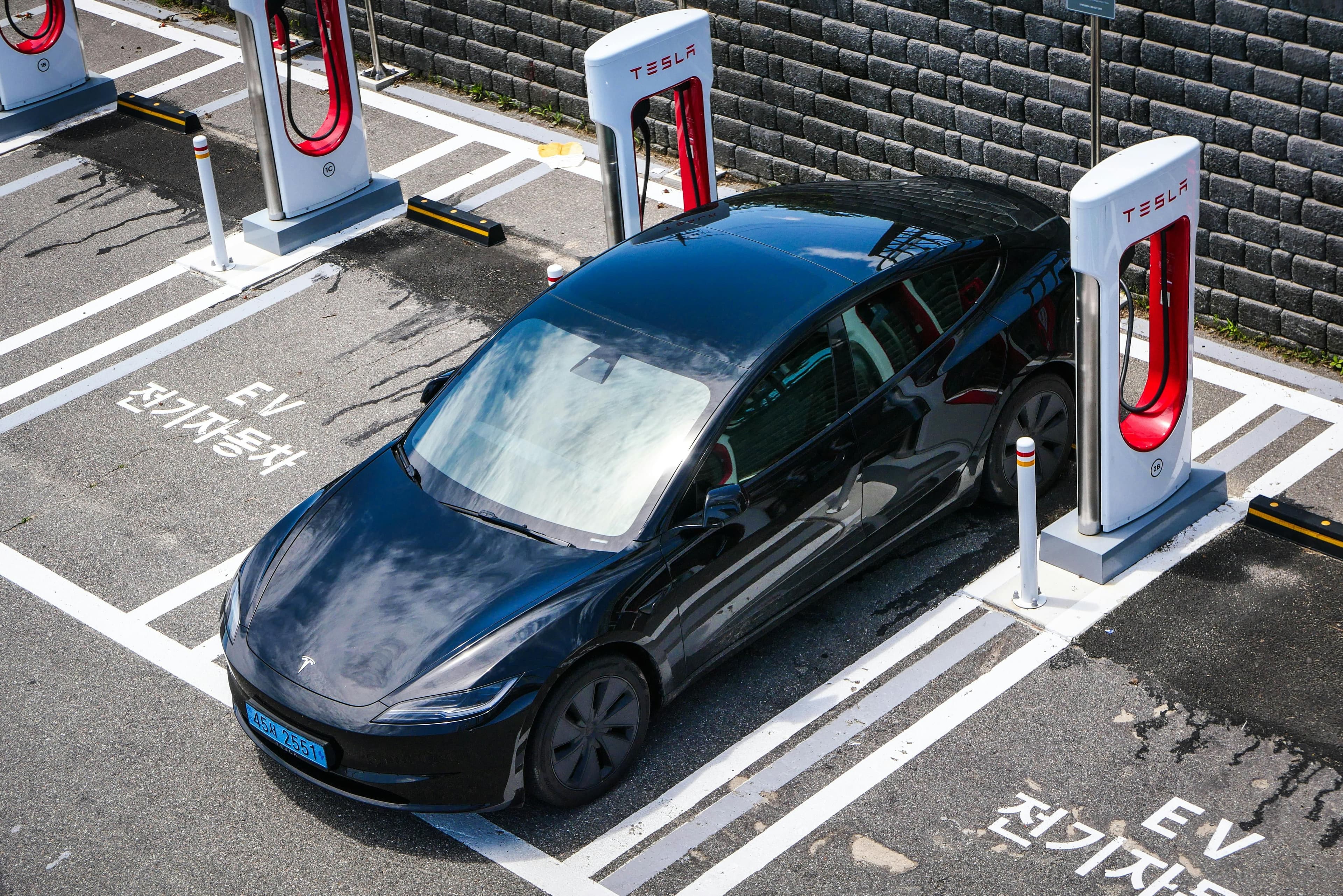 A black Tesla parked at a charging station in an urban setting.