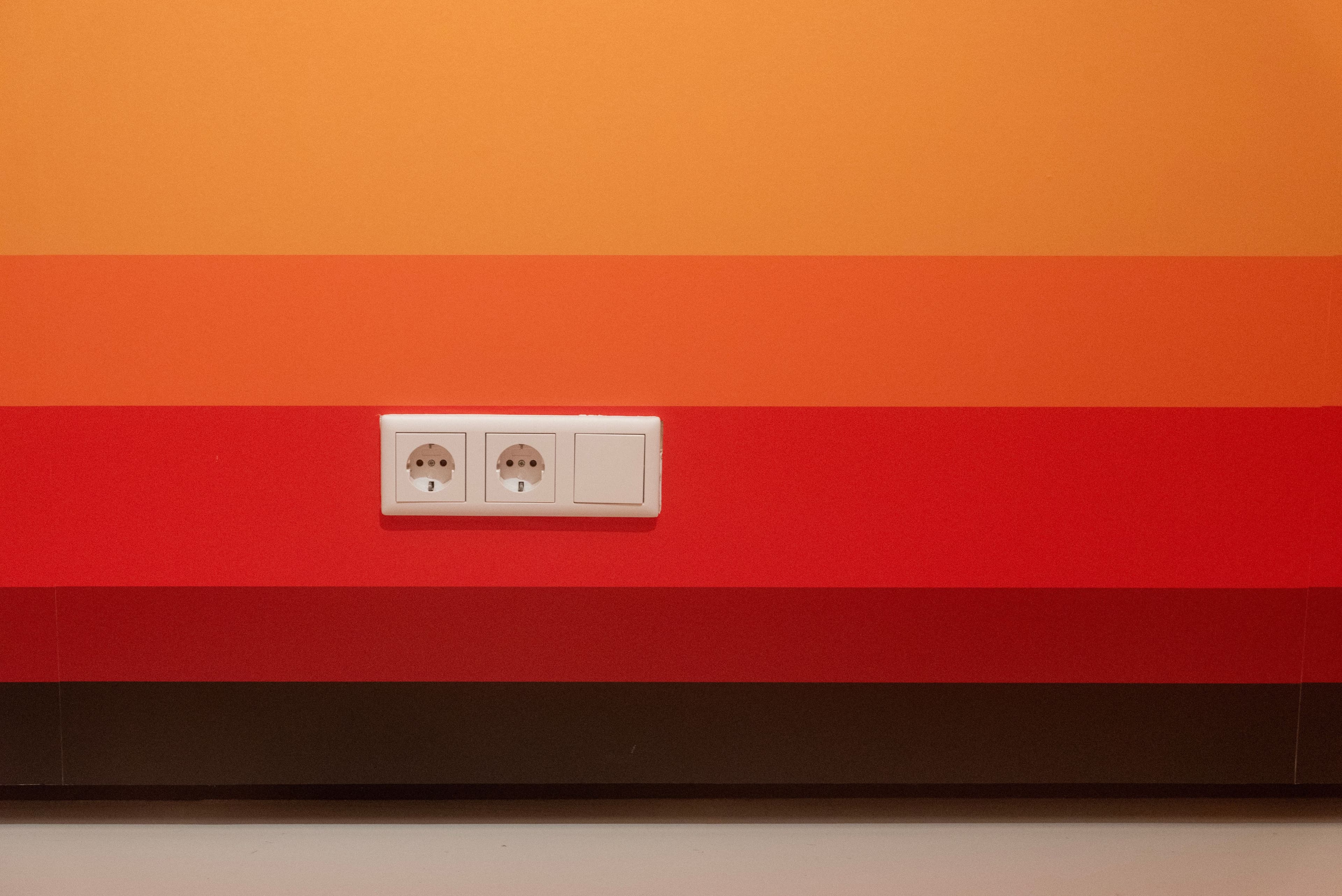 Minimalist design of orange and red striped wall with dual sockets.